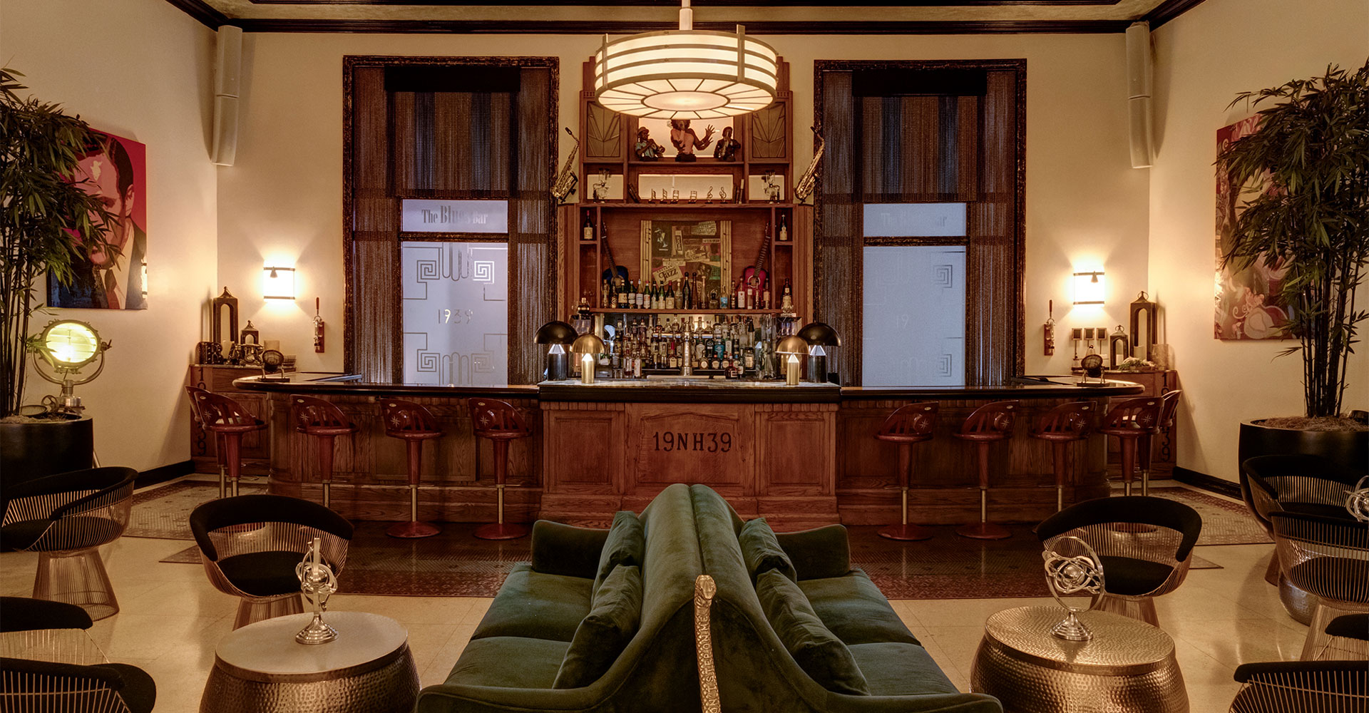 A dimly lit bar with a green sofa, wooden bar, stools, chairs, and tables.