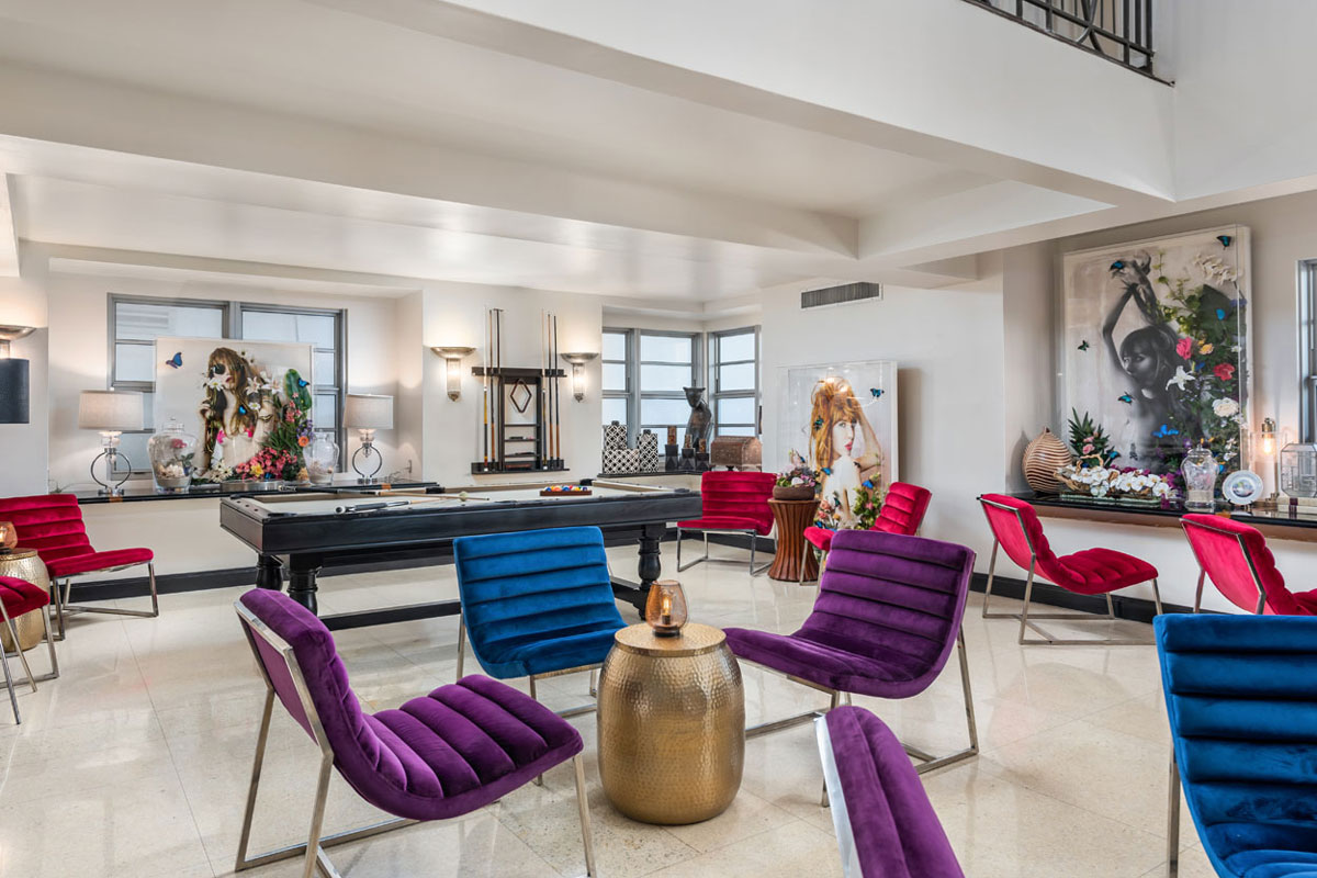 A brightly lit lounge with colorful velvet chairs, a pool table, and modern decor.
