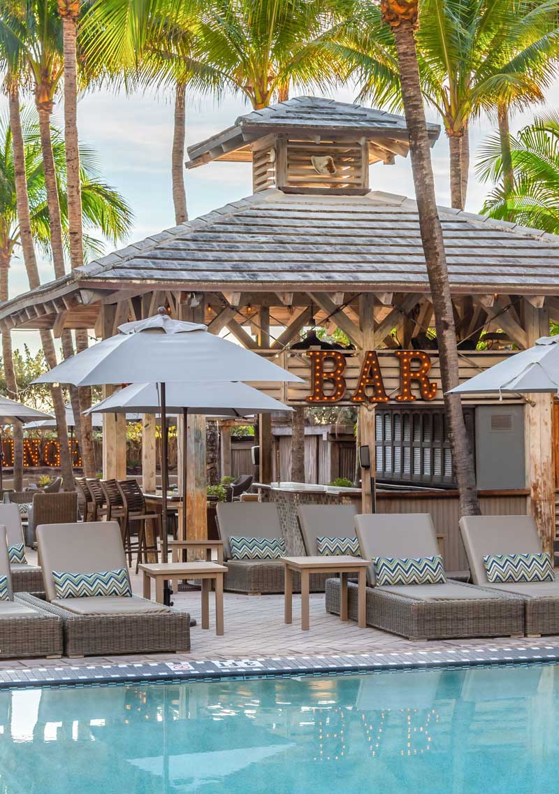 A poolside bar with lounge chairs and palm trees in the background.