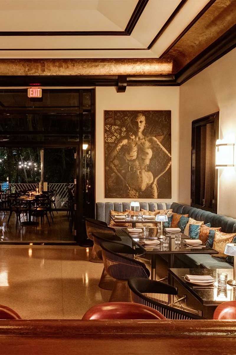 A dining area with a long couch, tables and chairs, and a large artwork on the wall.