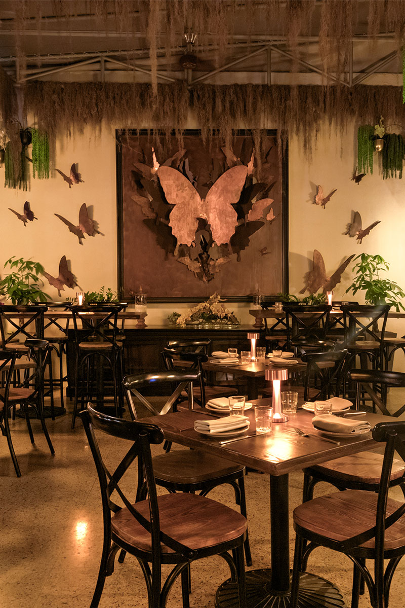 A dining area with tables and chairs, artwork on the wall, and plants.